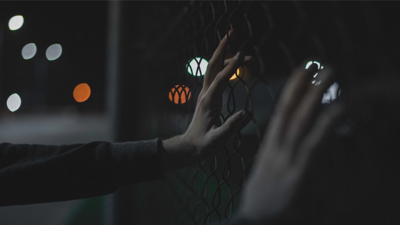 Hands holding a chain link fence