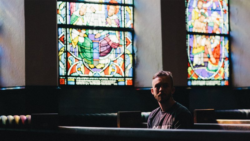 Man sitting in church pew in front of stained glass windows