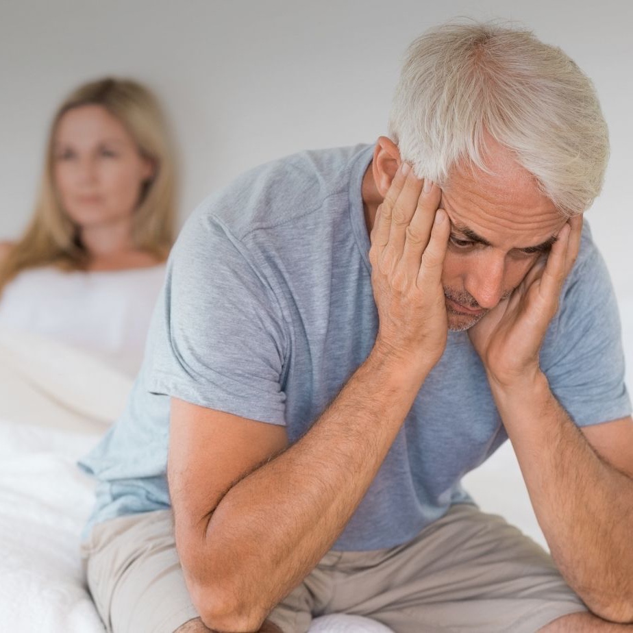 Bekymrad man sitter på sängkanten med sin kvinna sittandes bakom honom