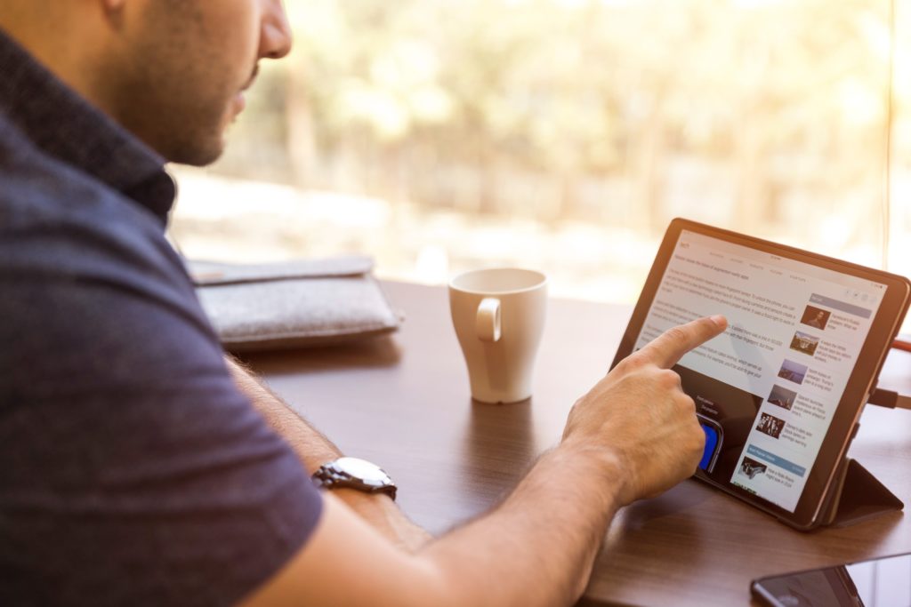 cropped-photo-of-man-sitting-at-table-with-coffee-mug-while-using-pointer-finger-to-navigate-on-propped-up-tablet