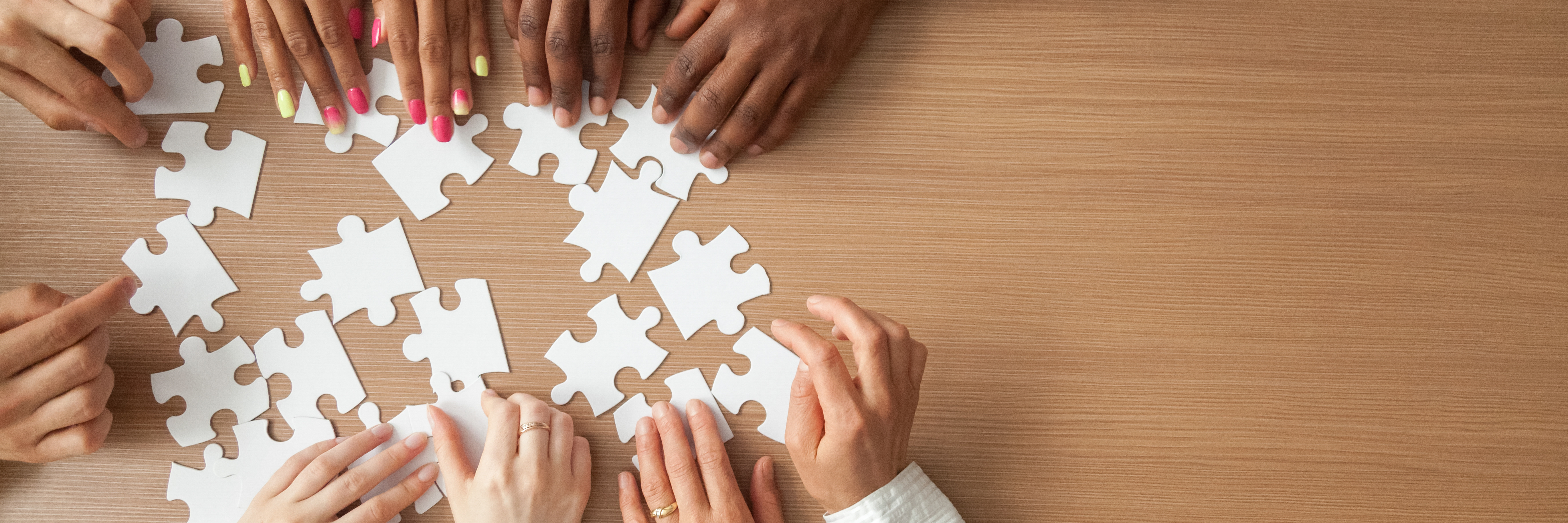people's hands assembling a puzzle together on a wooden table