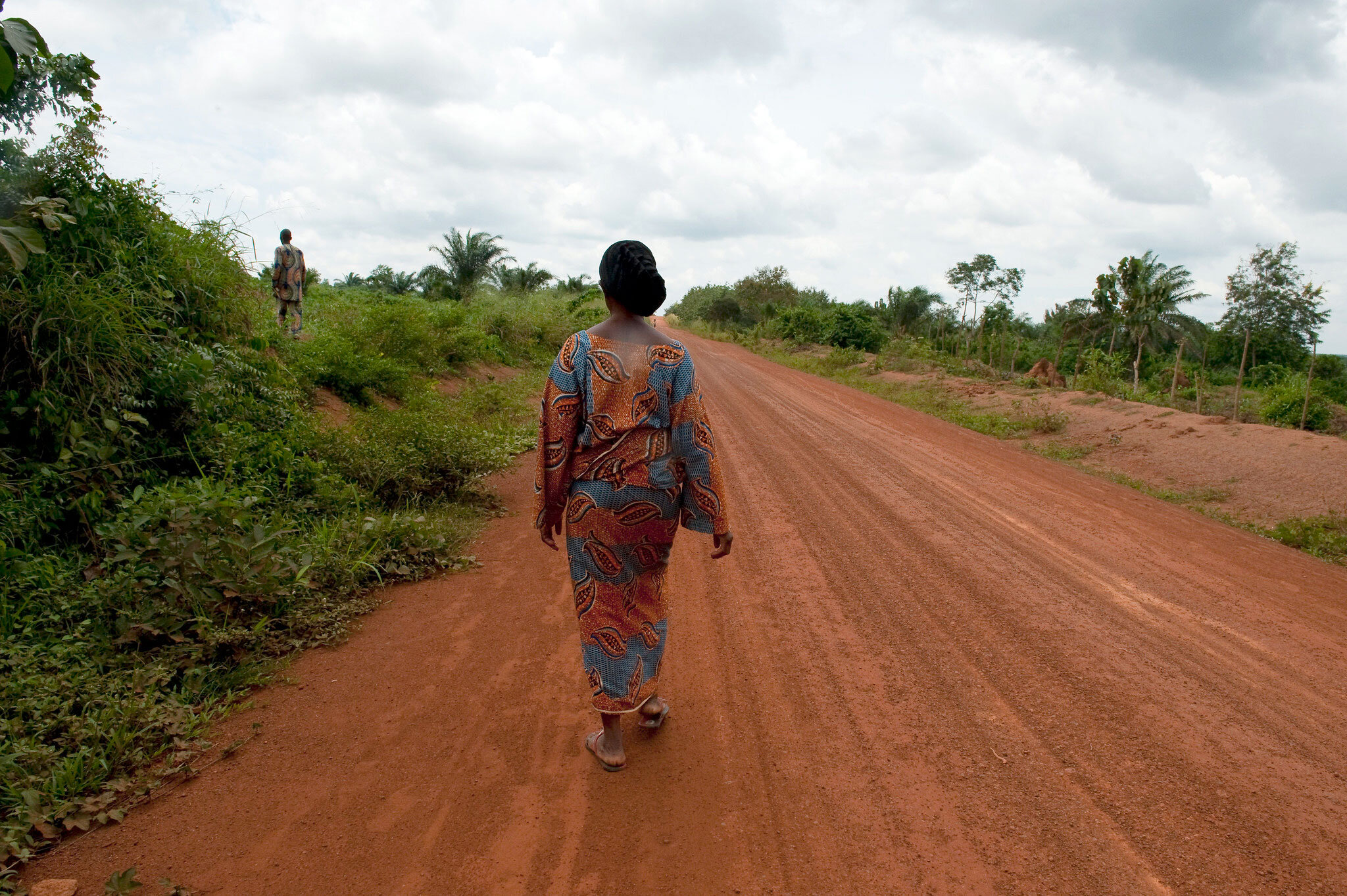 a woman in a dress and sandals walking down a dirt road