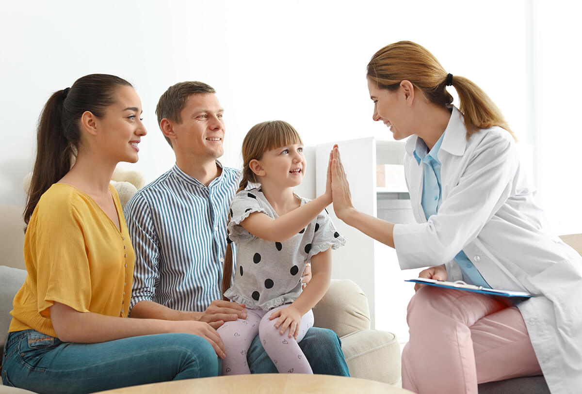 young girl sitting on her dad's lap touching hands with her ConciMed doctor during her primary care house call