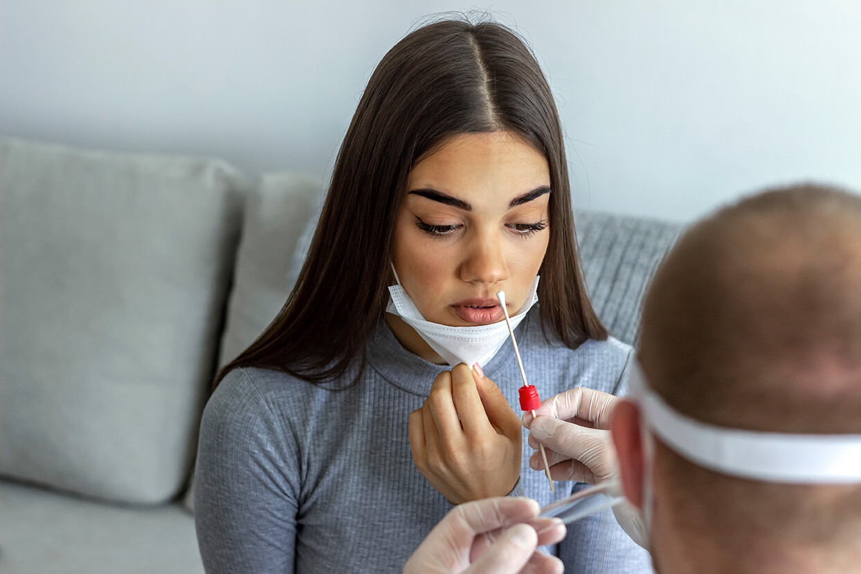 lab technician holding a nasal swab leaning to test a young woman with a mask for covid-19