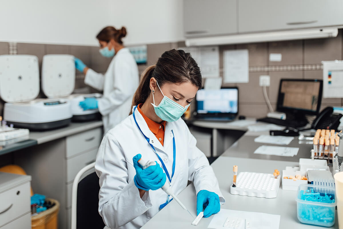woman wearing lab coat, face mask, and latex gloves in a laboratory processing a covid-19 test