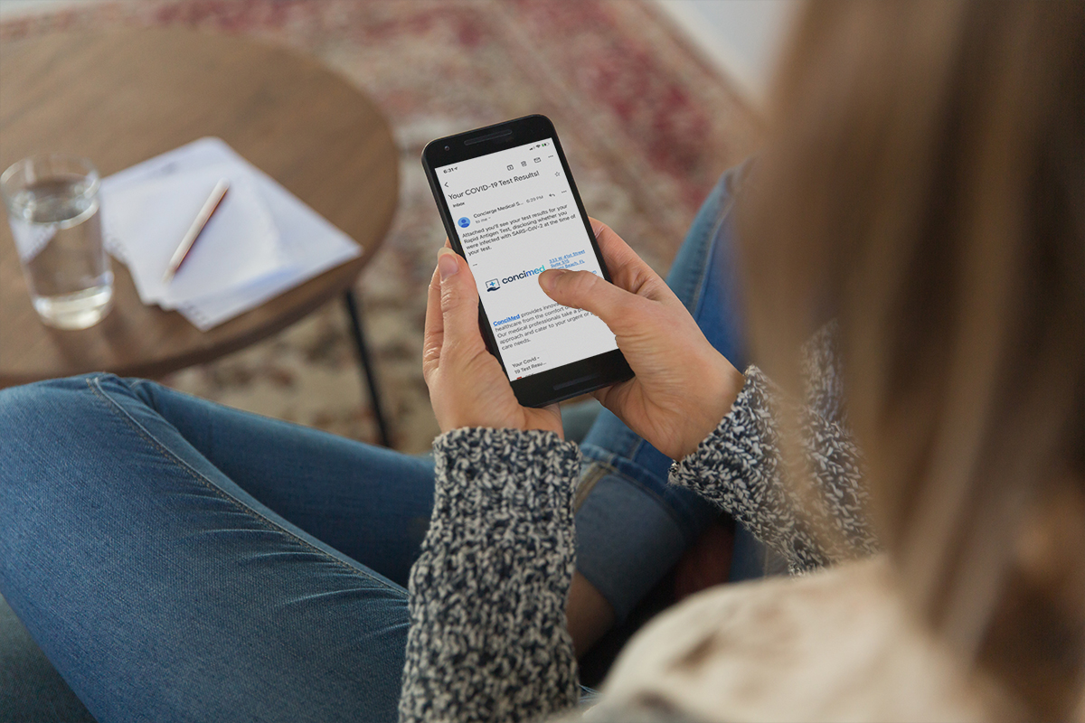 woman holding her phone with an email on it from ConciMed with her covid-19 test results