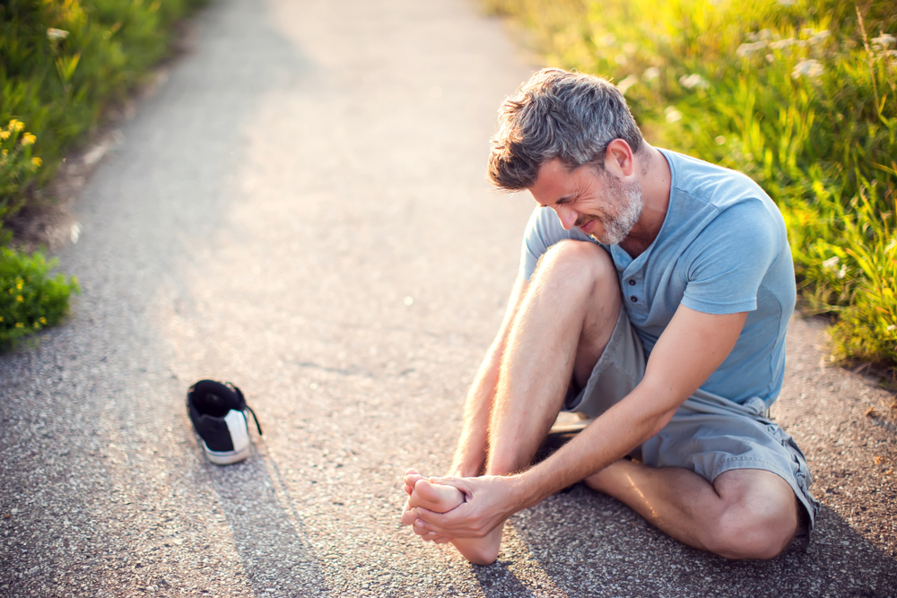 man on path sitting on floor holding his foot and wincing in pain as he considers seeing a podiatrist