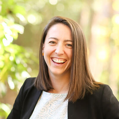 A picture of Emily Campion smiling at the camera with greenery behind her