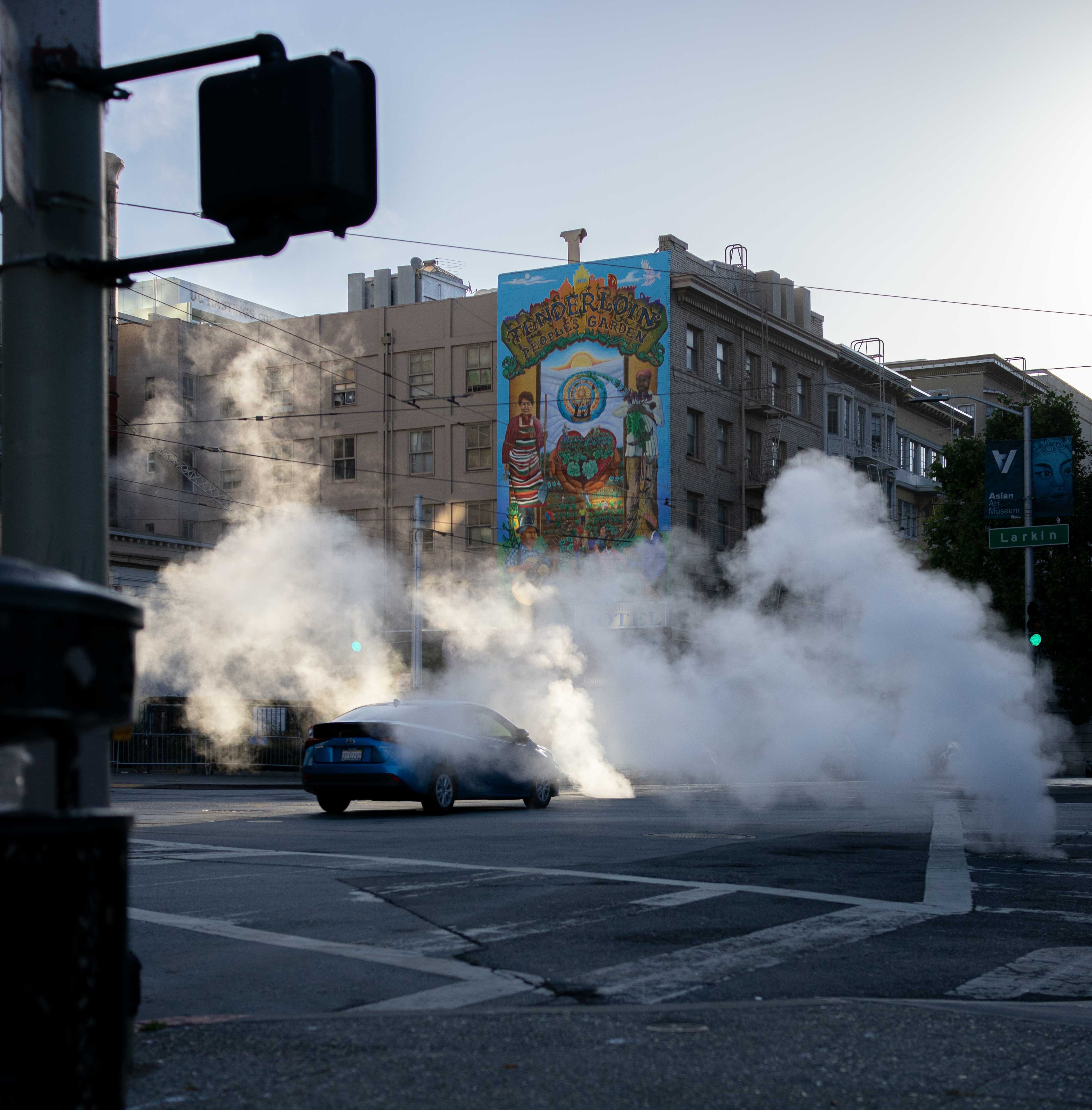 a black car surrounded by smoke in a city road