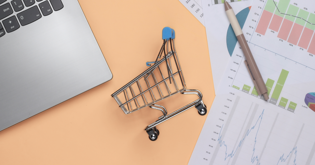 a shopping cart toy flat layed between a computer and a noting pad.