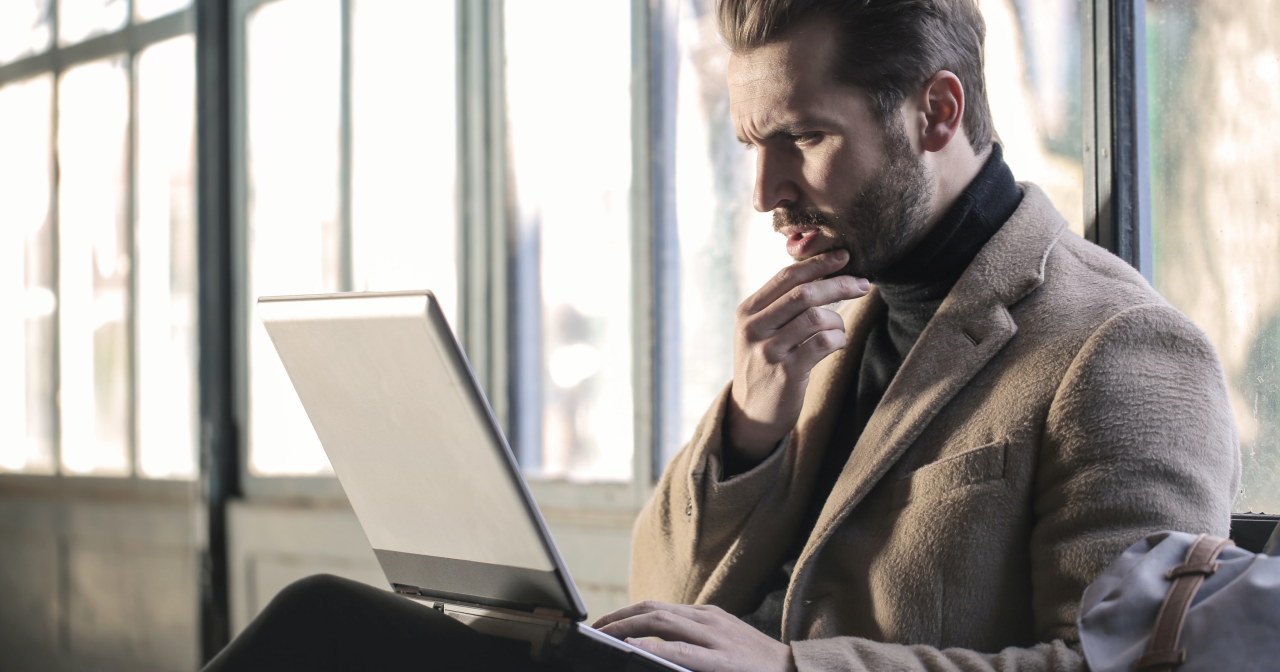 A guy in the business suit wondering about something in front of his laptop.