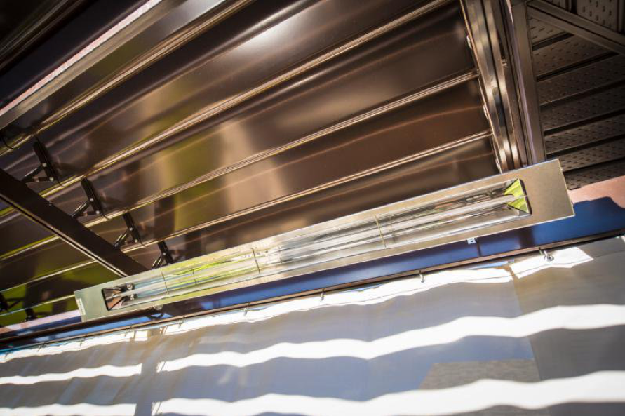 Chauffe-terrasse radiant électrique installé sous une pergola à lamelles rétractables en aluminium avec système de rideaux coulissants