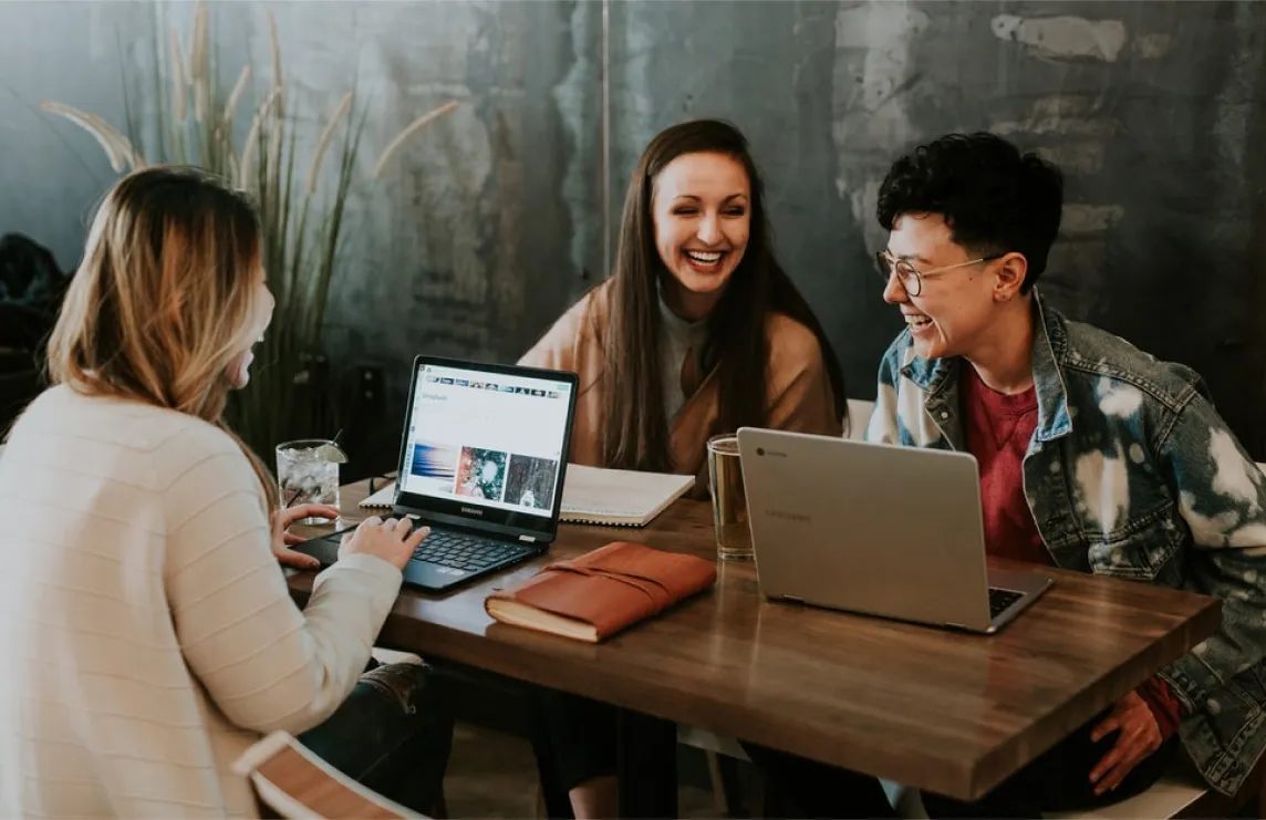 Group of young women sitting at table on laptops