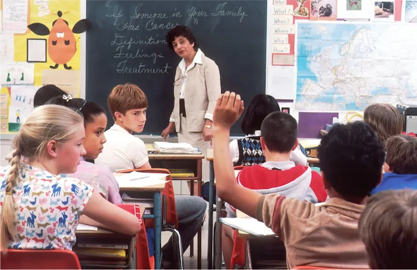 Students in classroom at their desks with one student raising his hand