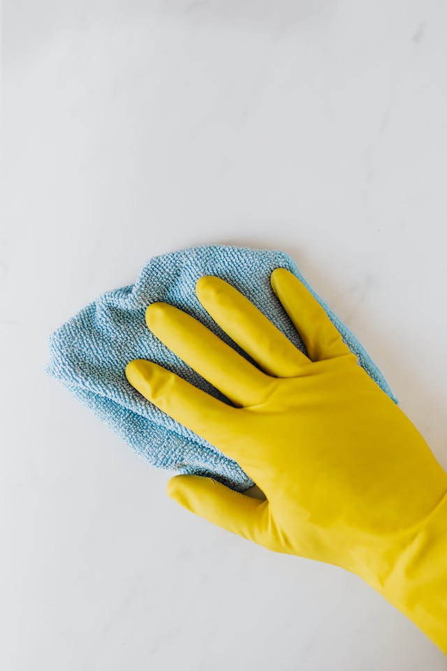 Person with yellow gloves cleaning a table with a blue cloth