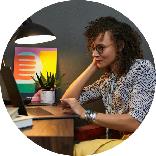 A woman sits at a computer on a table reserching maternity leave and family financial planning for freelancers.