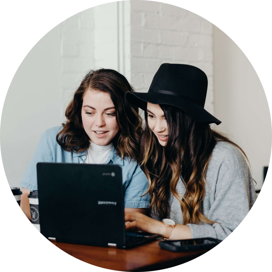 Two young women are sharing a laptop and are discussing what they see on screen