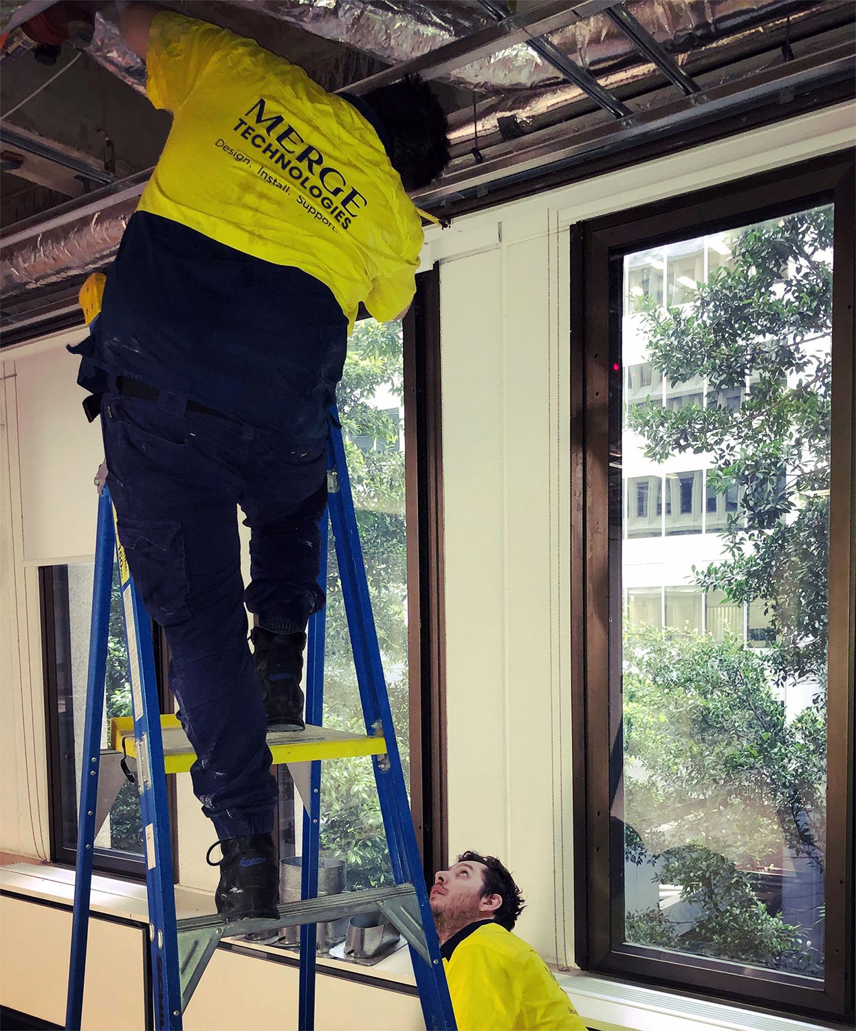Merge Technologies installers working on ladder installing Audio Visual equipment in office ceiling