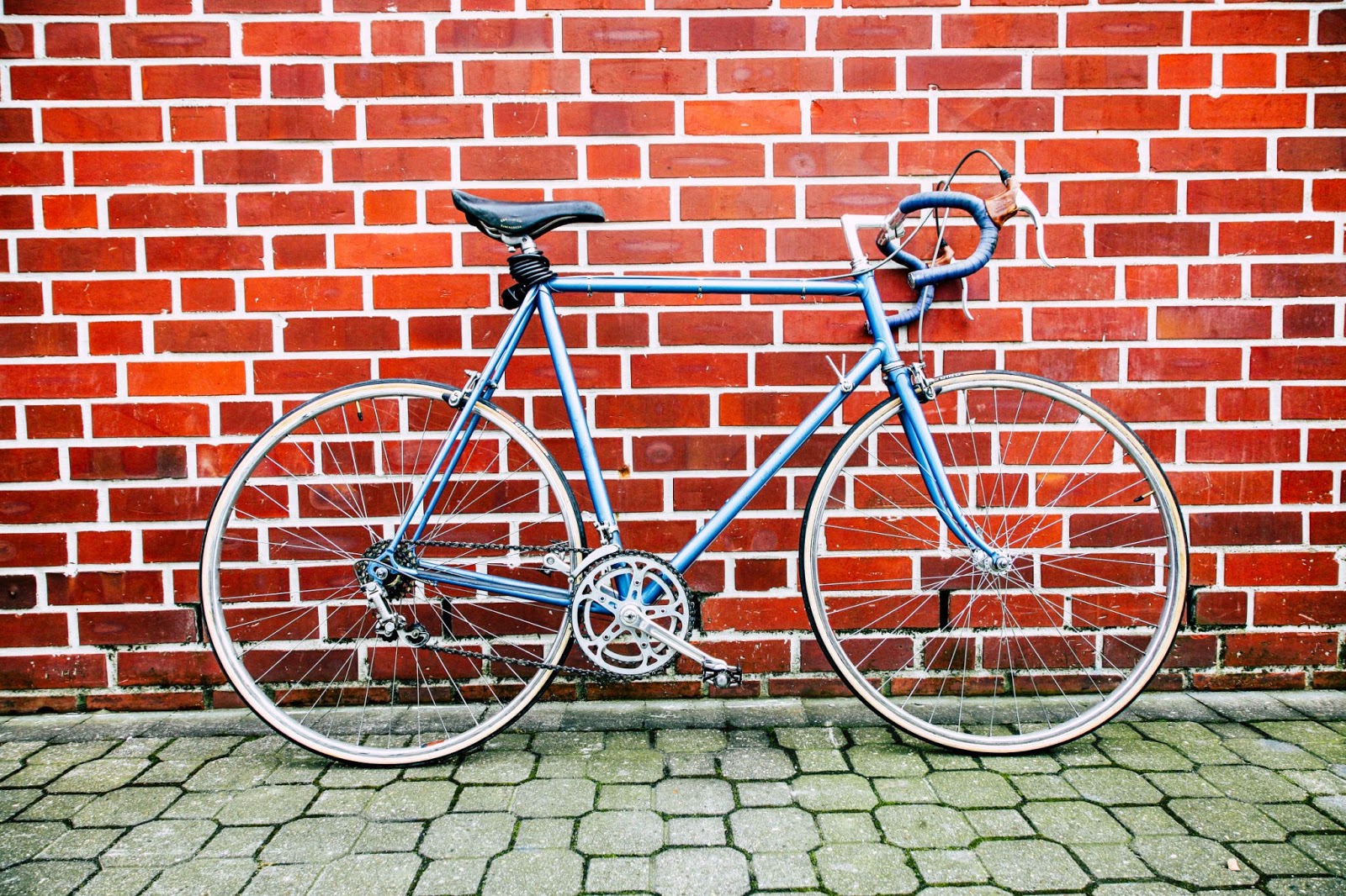 blue bicycle parked in front of a red brick wall