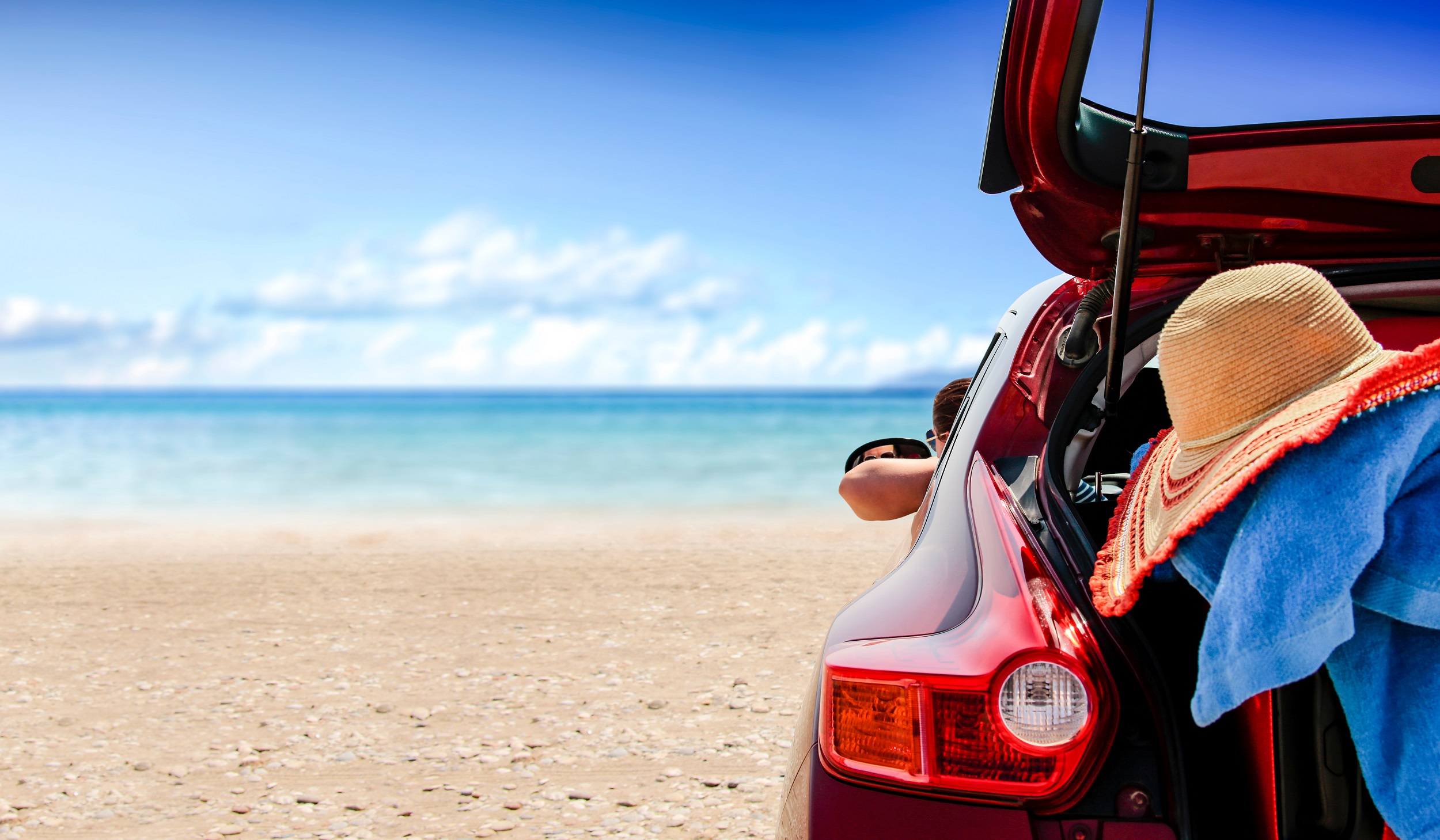 Rotes Auto steht am Meer am Strand mit offenem Kofferraum