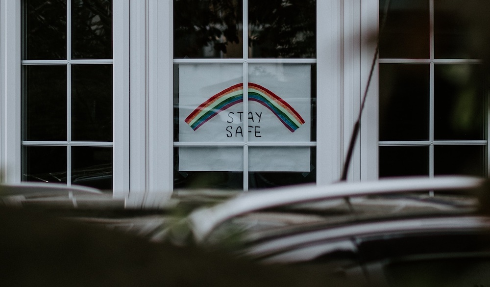 Child drawing of a rainbow in a window with a sign to "stay safe"