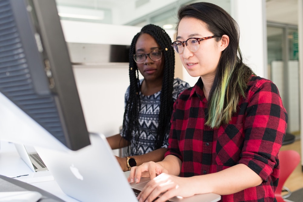 Two women working together in front of a computer screen.