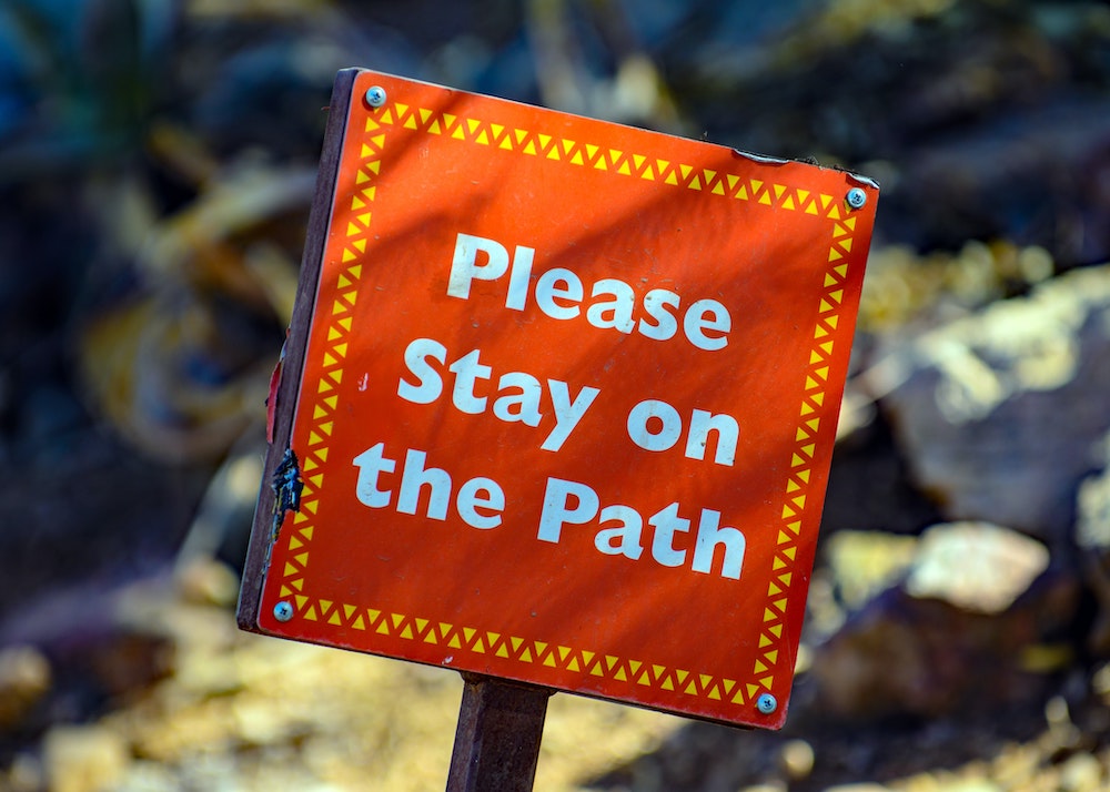 Red sign urging to stay on the path