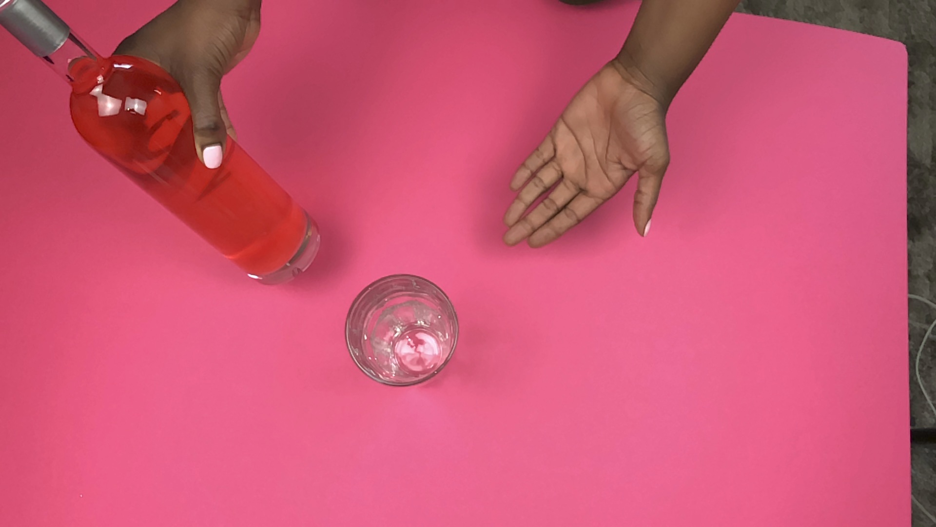 Melanated hand holding a vodka bottle and the other hand gesturing to a cup.