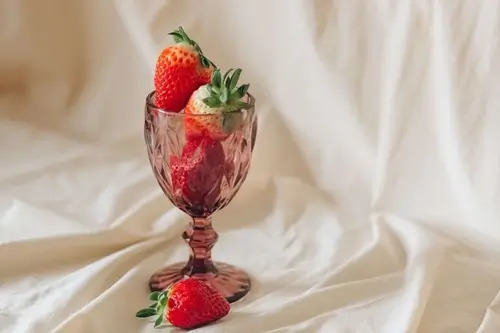 A purple glass goblet overflows with strawberries against a white cloth backdrop.