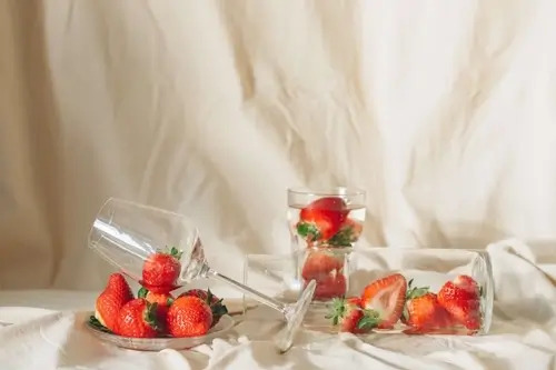 An empty wine glass lying on a bed of strawberries in front of a white cloth backdrop.