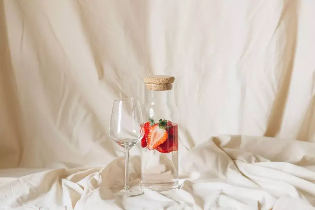 White cloth backdrop with strawberries in a bottle of water and an empty wine glass.