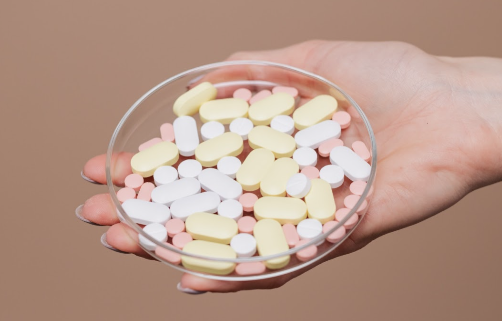 Hand holding assorted pills in a glass dish