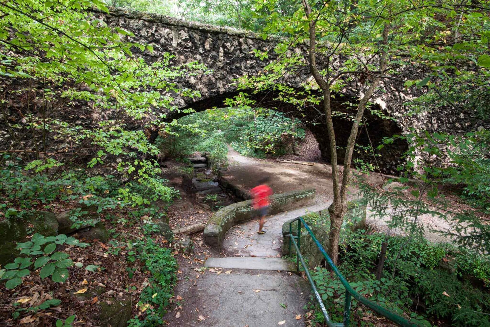 Man walking under stone bridge in park