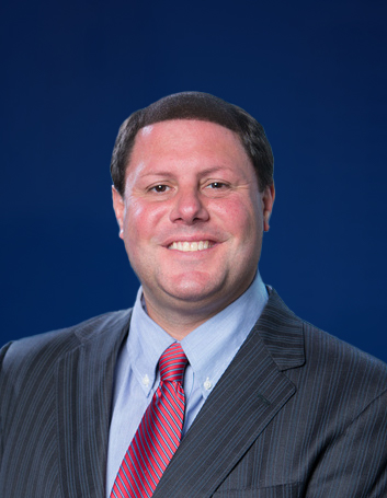 A headshot of Brook Scardina dressed in a suit and smiling