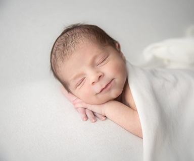 Photograph of newborn baby sleeping with white blanket on