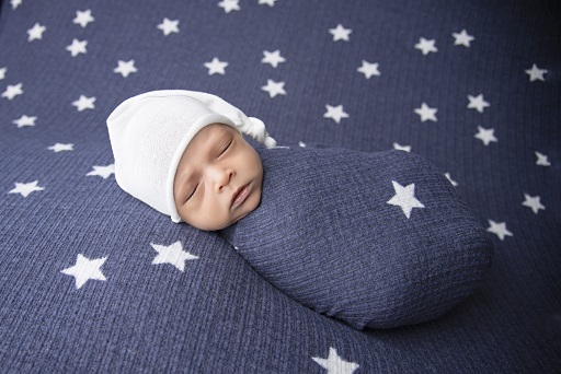 A photograph of a newborn baby swaddled in a blue blanket with white stars lying on the same blanket