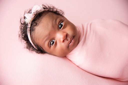 A photograph of a baby swaddled in a pink blanket with pink headband