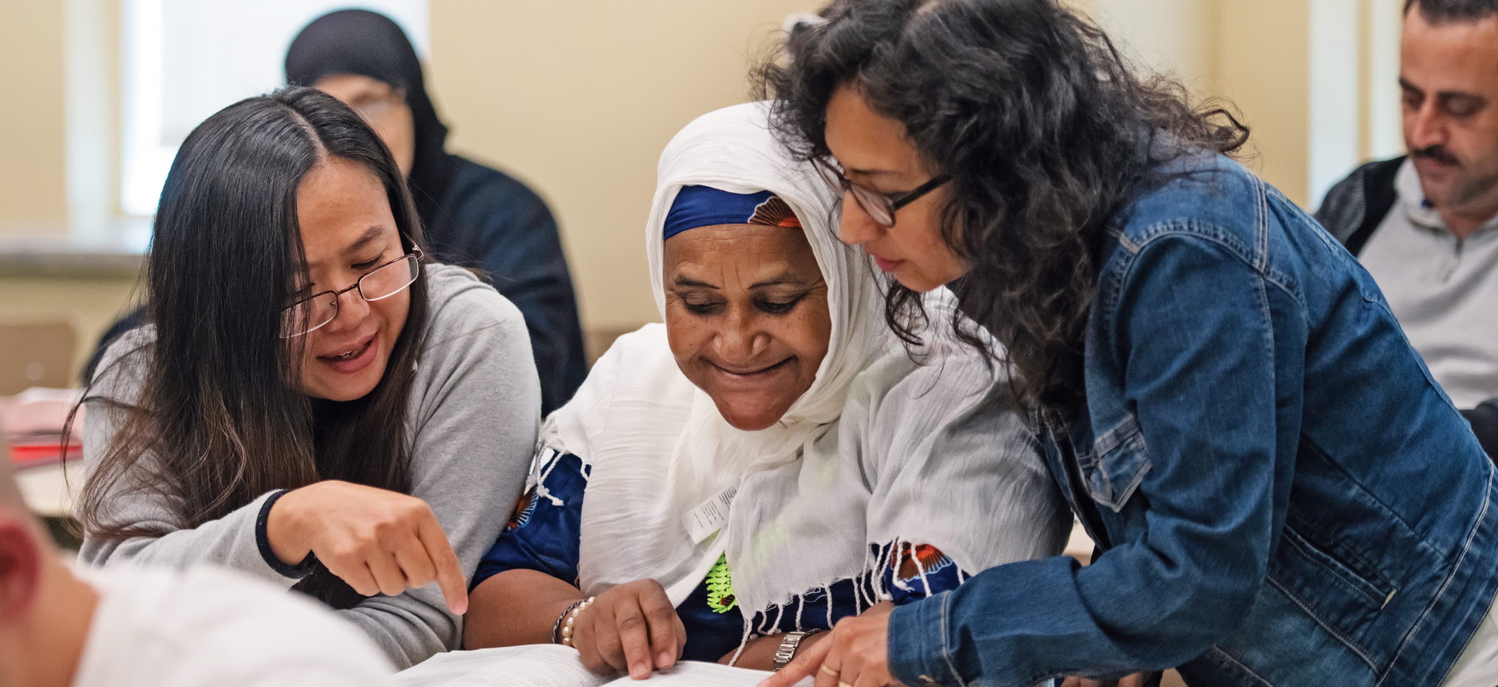 three women of various ethnicities reading a book together