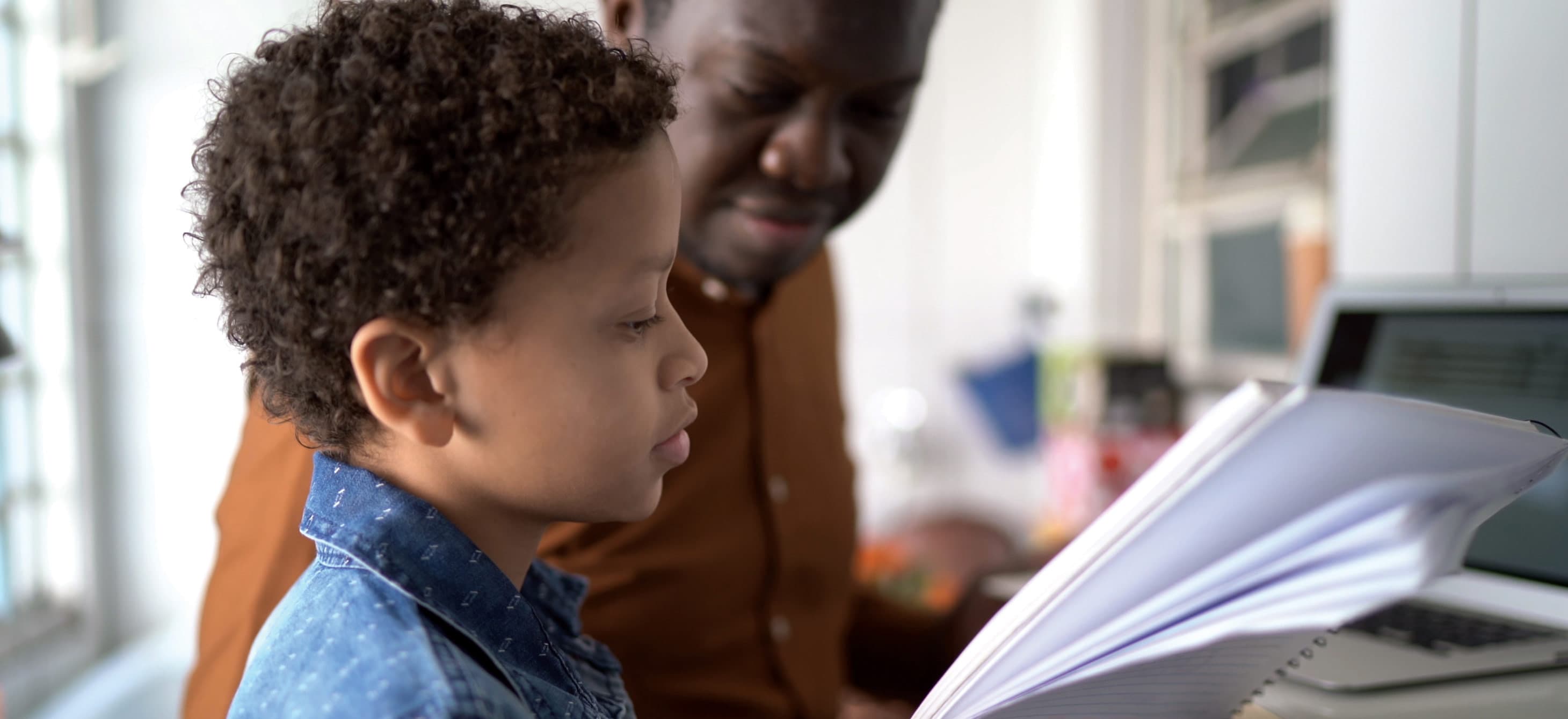 a boy looking at a lined notebook with an adult next to him