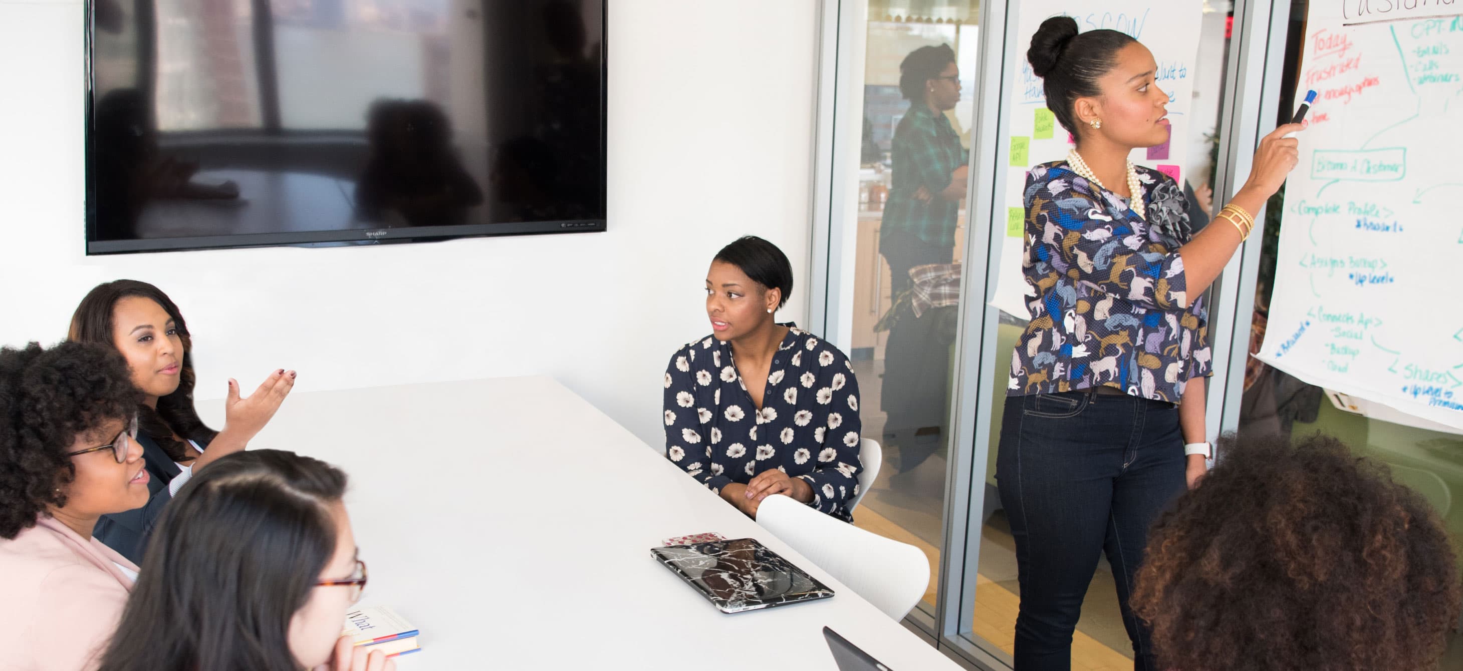a bright classroom with Black women around the table and one woman in front of a whiteboard