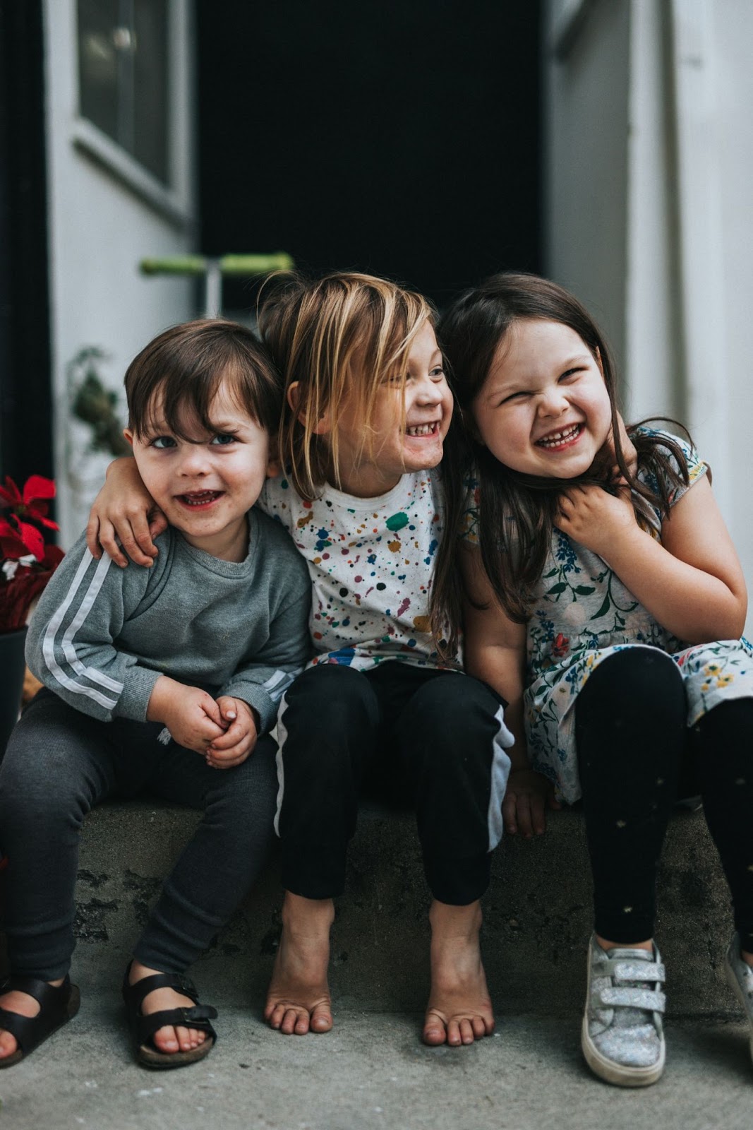 three children sitting down on a stoop and hugging