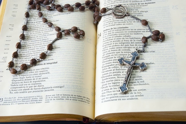 an open Bible, upon which rests a set of rosary beads.