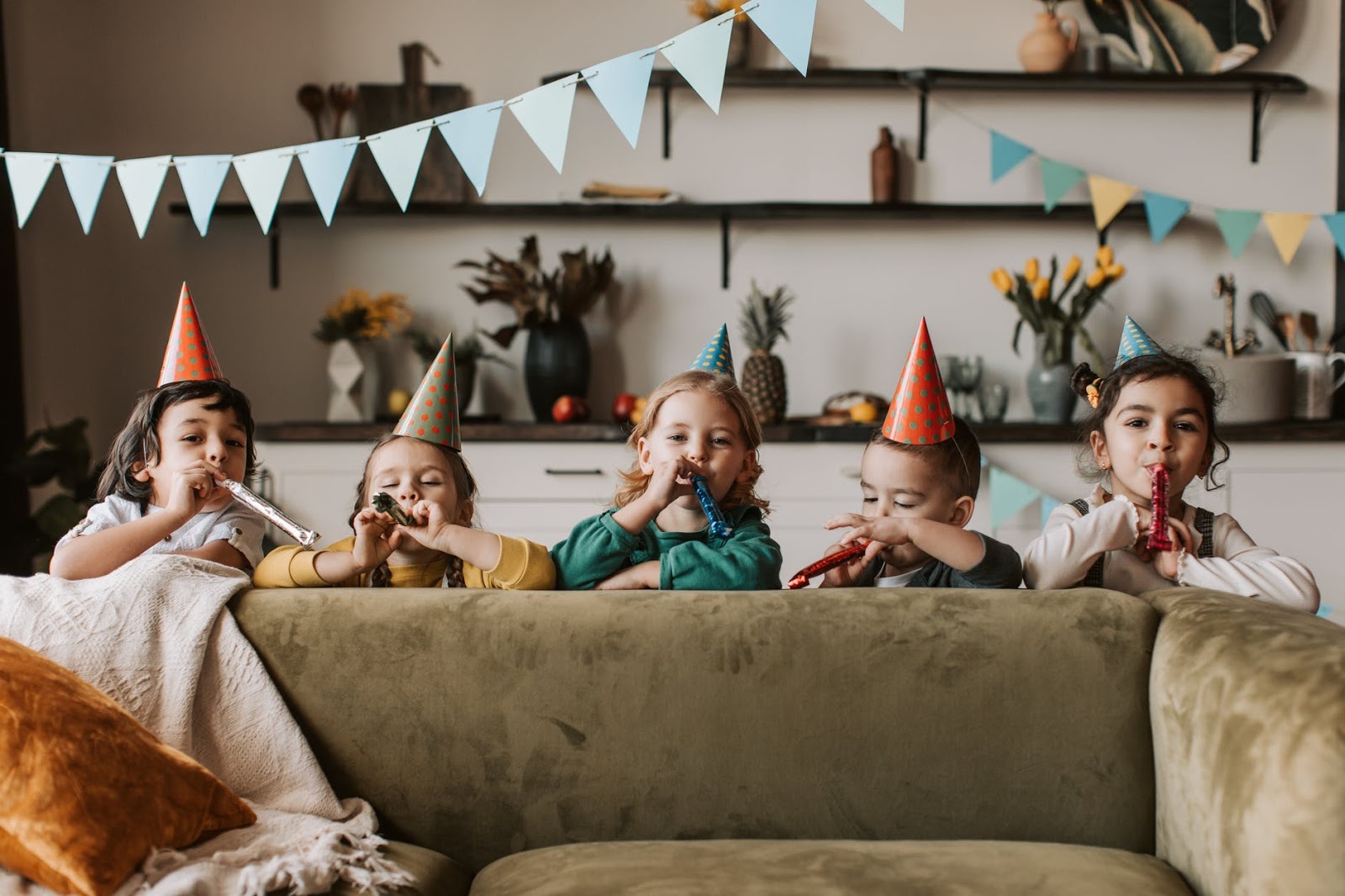 Five children stand behind couch with birthday decorations
