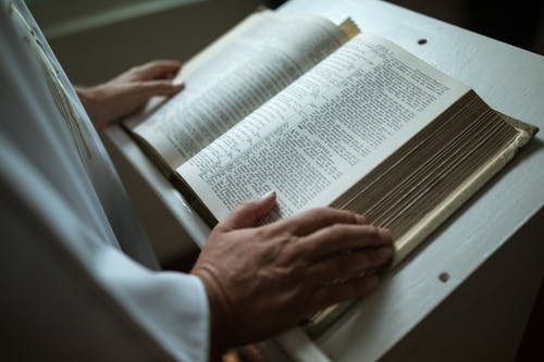 Bible sitting open on a stand with a person's hands on it.