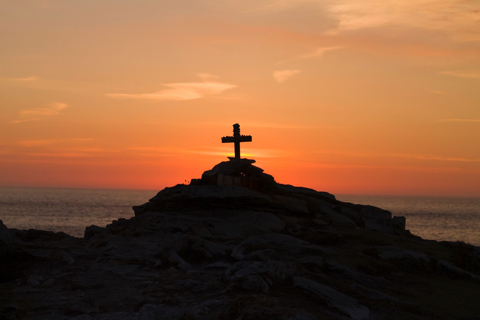 A cross on a cliff over the ocean at sunset