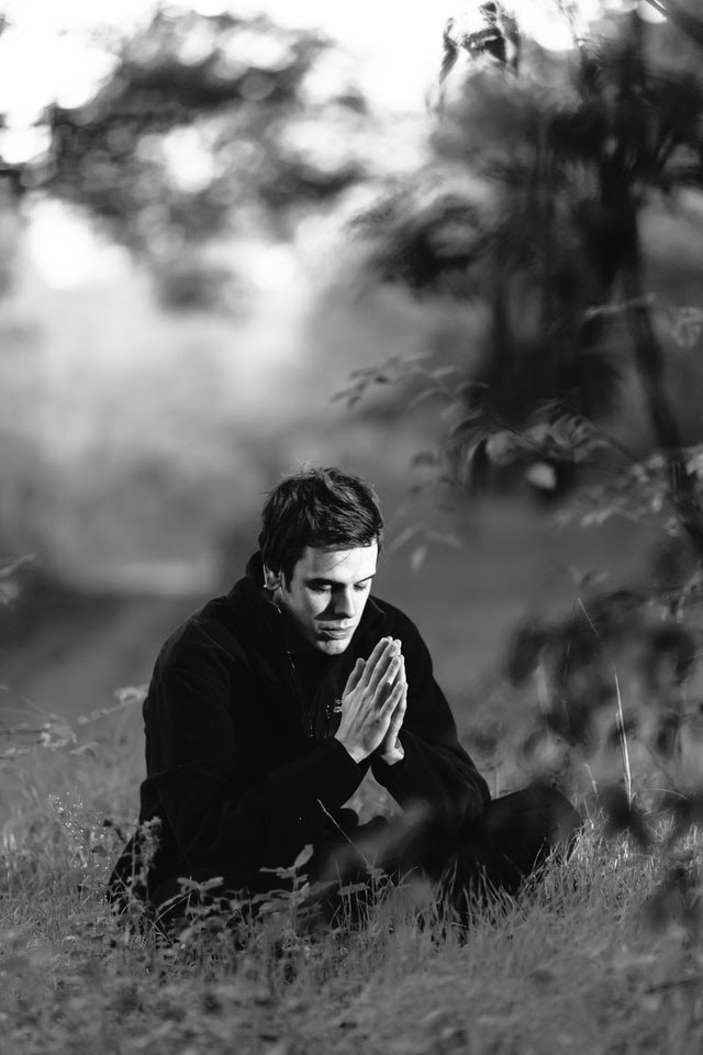 Young man meditating in a field, hands clasped in prayer