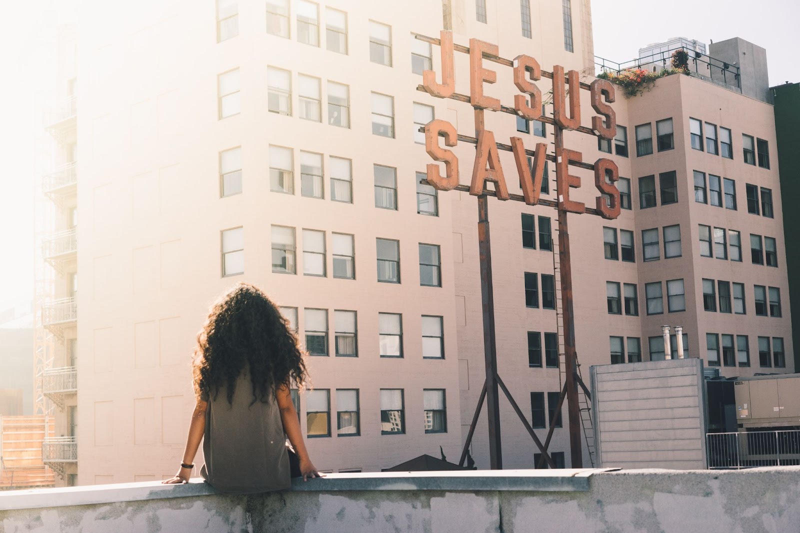 Girl sitting on a wall under a sign that says 'Jesus Saves'