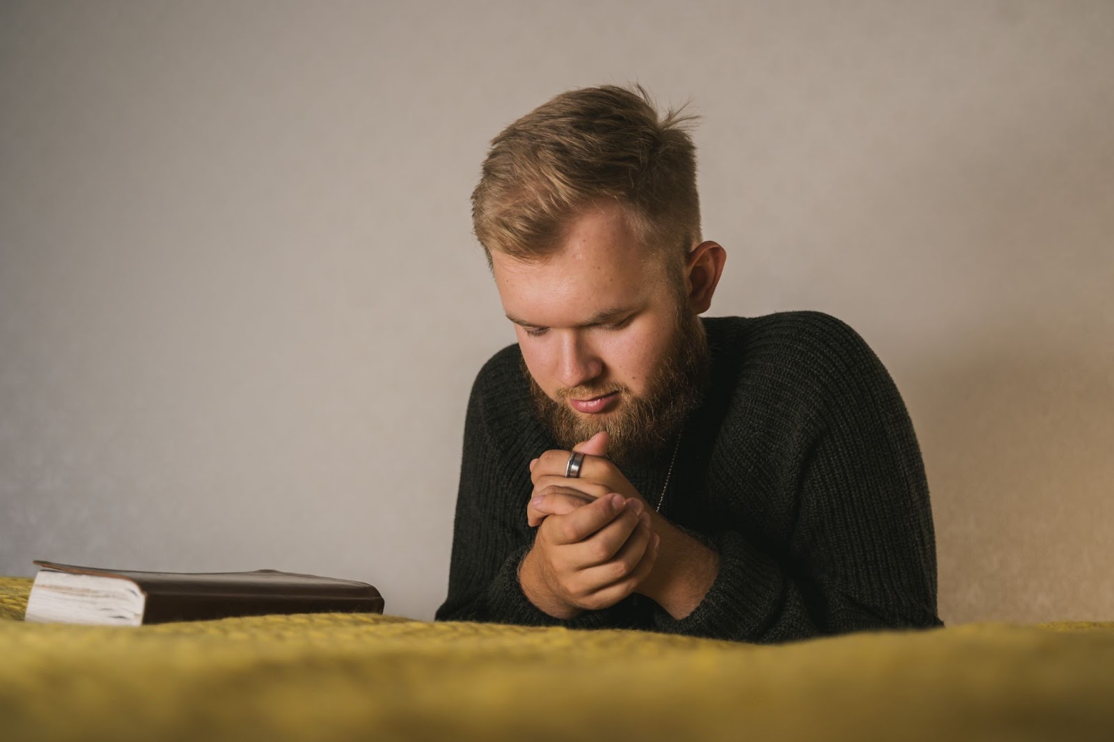 A young man prays at his bedside with a Bible