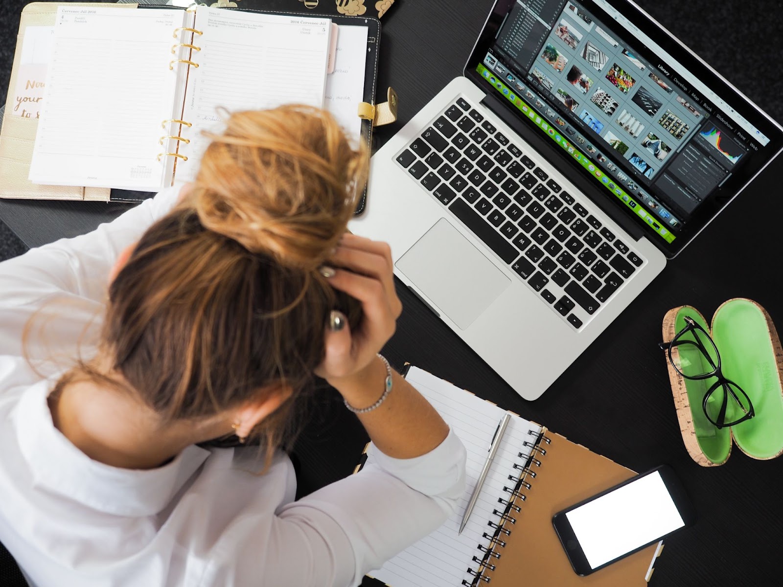 Woman stressfully holding her head surrounded by notepads and a macbook