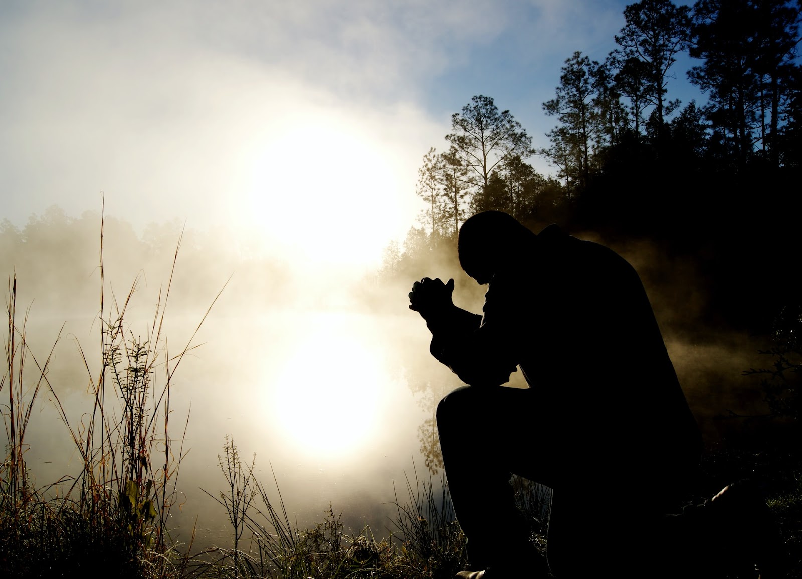 silhouette of a man praying by a lake